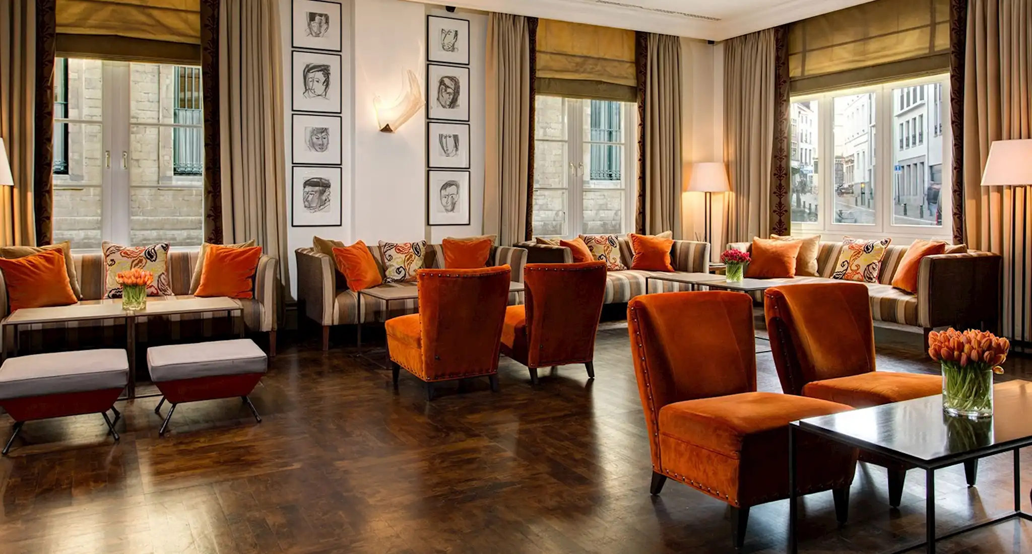 the lobby of amigo hotels in brussels features orange chairs and tables, creating a warm and inviting atmosphere.