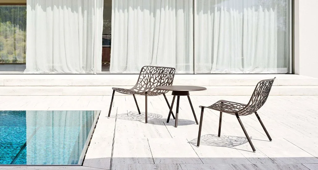two poolside chairs and a table set against a serene backdrop of a shimmering pool.