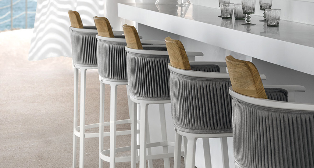 nicolette bar stool is a contemporary outdoor bar stool with aluminium and teak structure and fabric back and seat. nicolette is suitable for hospitality and contract projects.
