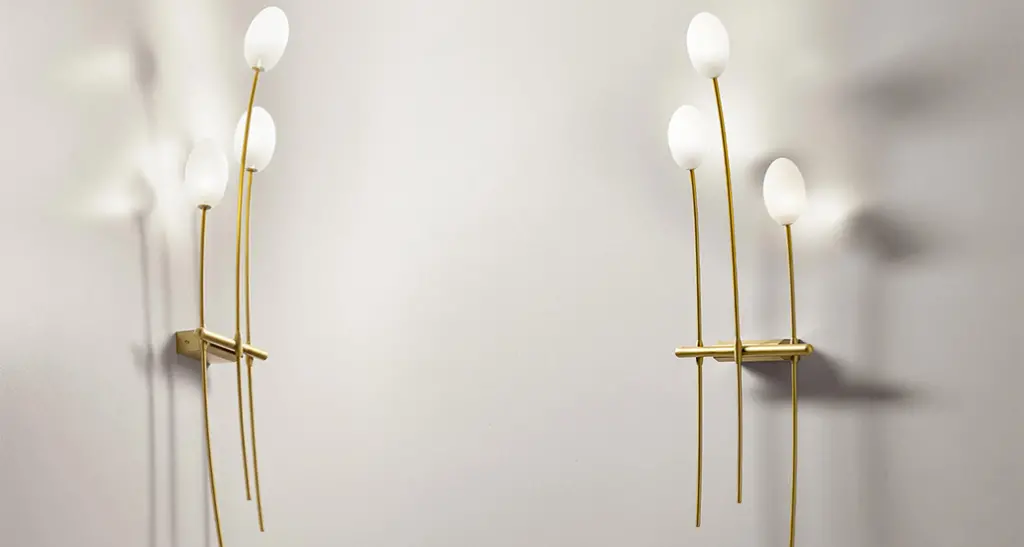 roris wall lamp is a LED contemporary wall lamp with metal frame and glass and is suitable for hospitality and contract spaces. Hers Roris is exuding a golden light and is placed in residential room with a mirror.